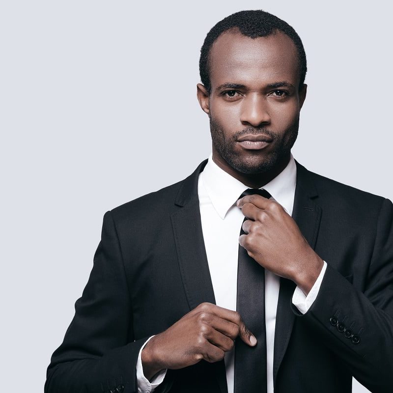 Perfect businessman. Portrait of confident young African man adjusting his necktie while standing against grey background