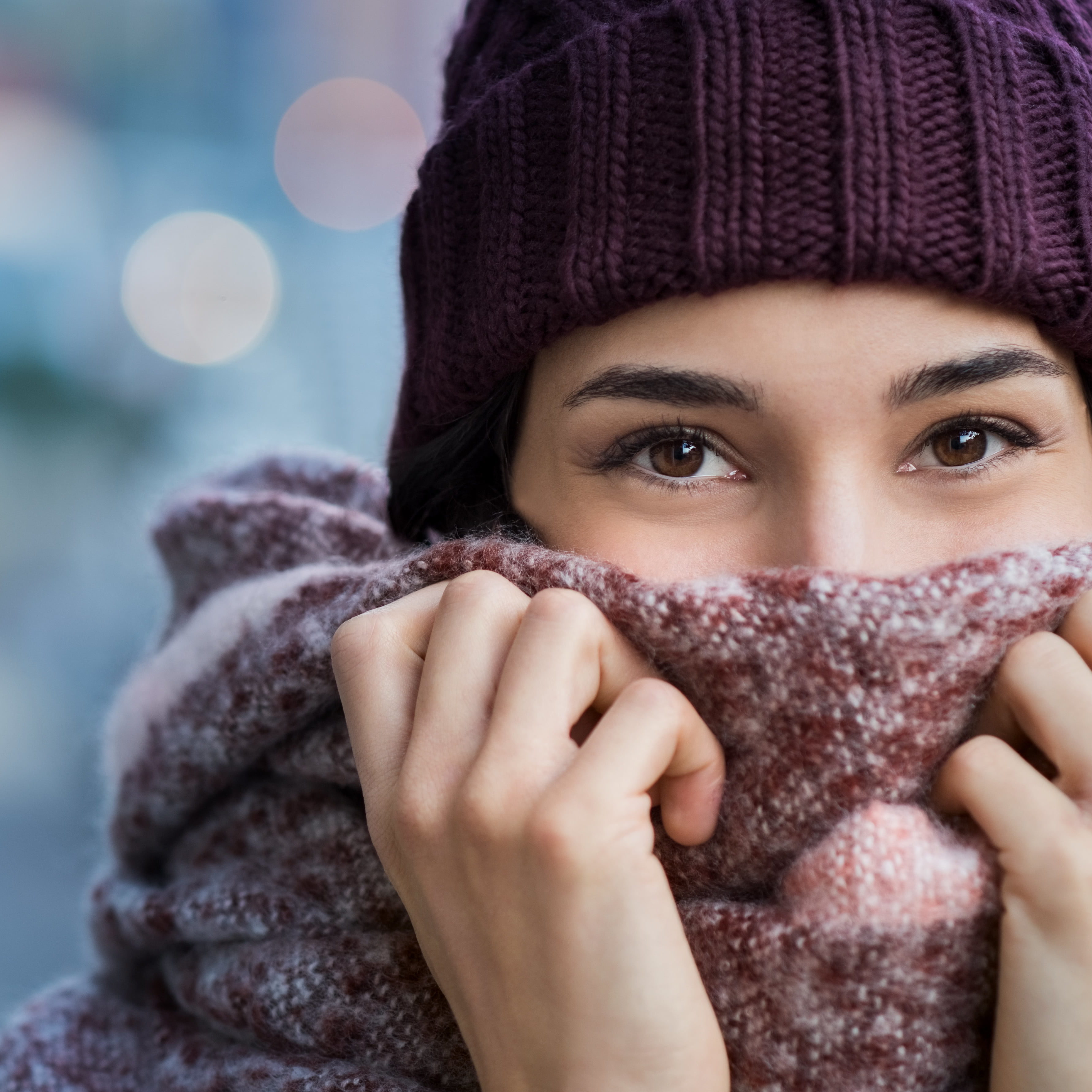 Woman feeling cold in winter Winter portrait of young beautiful woman covering face with woolen scarf. Closeup of happy girl feeling cold outdoor in the city. Young woman holding scarf and looking at camera."r